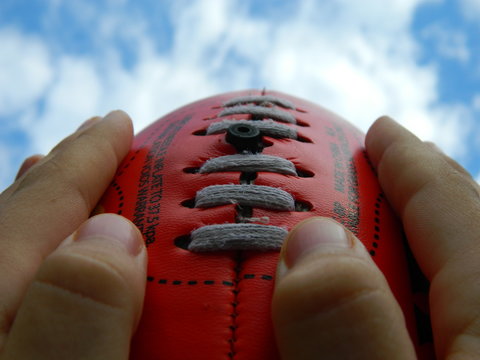 Two hands holding a red football on a sky background