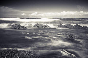 close up on beautiful sandy beach with rocks on atlantic coast in bidart in long exposure in black and white, basque country