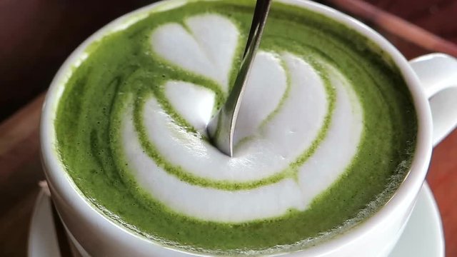 Little spoon diving into a creamy foam over a matcha latte