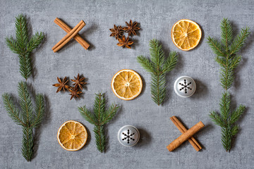 Christmas noughts and crosses deco with dried oranges, aniseeds, cinamon sticks, fir tree branches and silver bells on grey background