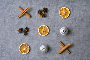 Christmas noughts and crosses deco with dried oranges, aniseeds, cinamon sticks and silver bells on grey background