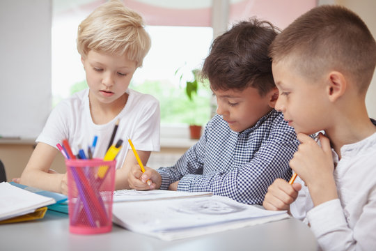 Childhood, Communication Concept. Group Of Little Kids Working On Art Project Together. Two Schoolboys And A Girl Sketching For Art Class Homework