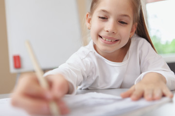Cropped shot of a lovely happy young girl concentrating, drawing or writing in her textbook, copy space. Children education, development concept