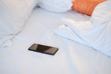 Smartphone blank white screen on the messy bed, smartphone concept.