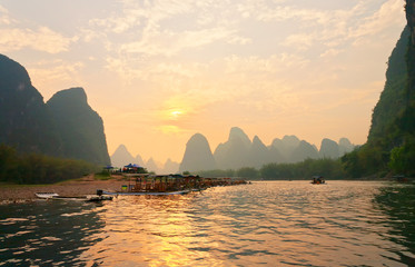 China. Yangshuo. Beautiful Li (Lijiang) River with green karst hills at sunset. Tourists travel along the river on traditional bamboo rafts and admire the setting sun in an unusual natural park - obrazy, fototapety, plakaty