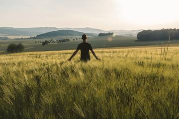 Young man stand in rural czech landscape with wheat field, hill and trees at sunset