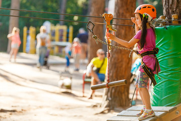 Obraz na płótnie Canvas Happy school girl enjoying activity in a climbing adventure park on a summer day
