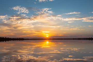 Fototapeta premium Sunset reflection lagoon. beautiful sunset behind the clouds and blue sky above the over lagoon landscape background. dramatic sky with cloud at sunset