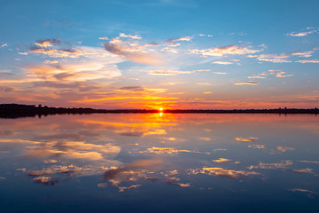 Naklejka na ściany i meble Sunset reflection lagoon. beautiful sunset behind the clouds and blue sky above the over lagoon landscape background. dramatic sky with cloud at sunset