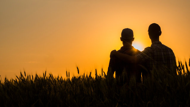 Two Young Men Hugging Against The Backdrop Of The Sunset, Looking Forward To The Horizon