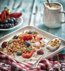breakfast granola yogurt, strawberry, blueberries, raspberries on a white plate. on a blue table board with a towel	