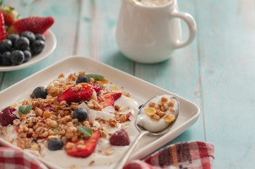 breakfast granola yogurt, strawberry, blueberries, raspberries on a white plate. on a blue table board with a towel	