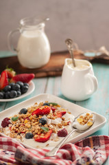 breakfast granola yogurt, strawberry, blueberries, raspberries on a white plate. on a blue table board with a towel	