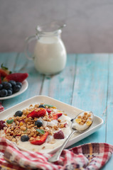 breakfast granola yogurt, strawberry, blueberries, raspberries on a white plate. on a blue table board with a towel	
