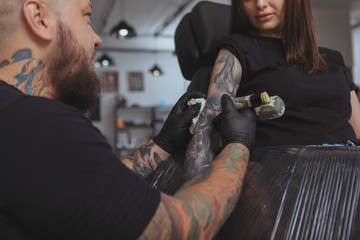 Cropped shot of a beautiful woman getting her arm tattooed by professional tattoo artist. Rear view...
