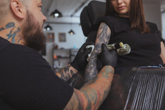 Cropped shot of a beautiful woman getting her arm tattooed by professional tattoo artist. Rear view shot of a tattooer making tattoo on female client arm