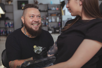 Cropped shot of a excited tattoo artist laughing, talking to his client while doing a tatoo on her...