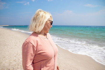 Happy life. Adult blond woman walking on the beach of the ocean on a sunny day. Happy life