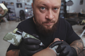 Cropped close up fish eye shot of a serious tattoo artist looking to the camera while working on a...