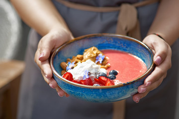 Morning breakfast in a blue plate in the hands of a waitress. fresh blueberry smoothies for breakfast bowls of nuts, seeds and fruit. selective focus. Healthy breakfast.