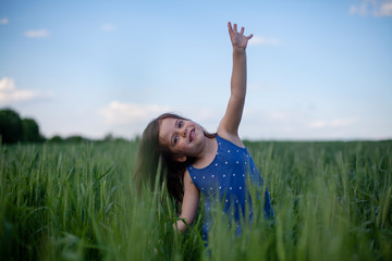 Naklejka na ściany i meble Happy girl walking in green wheat, enjoying the life in the field. Nature beauty, blue sky and field of wheat. Freedom concept