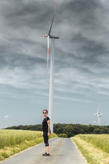 einzelne Frau steht auf Teerweg vor einer Windkraftanlage