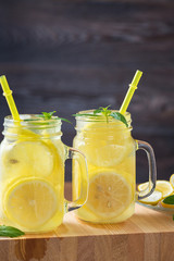 Lemonade in a jar with ice and mint on a black wooden table.