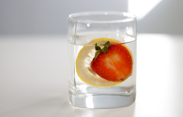 red strawberry and lemon in glass water lemonade side view close-up on white background