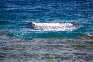 Fototapeta premium Blue clear water. Beautiful blue sea wave photograph close up. Beach vacation at sea or ocean. Background to insert images and text. Tourism, travel. Big wave with a white hat