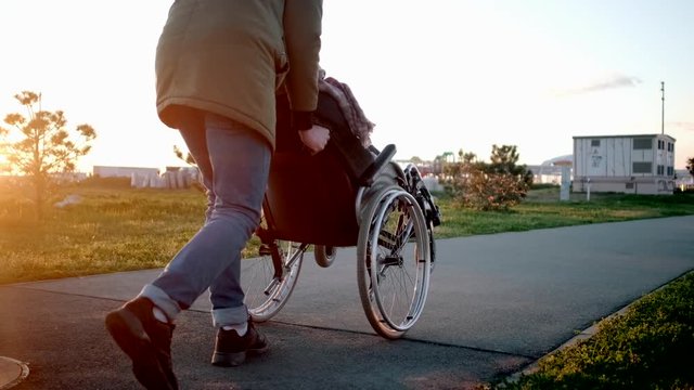 Careful man is rolling invalid carriage with woman in garden, lifting wheels