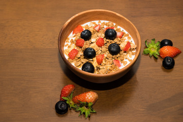 Fresh corn flakes cereal and fruits strawberry and blueberry in wood bowl