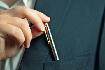  businessman in a suit taking or putting  a pen from the breast pocket of his jacket