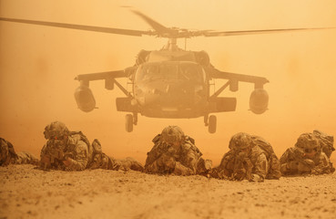 Military soldiers in front of helicopter between storm and dust in battle field.
