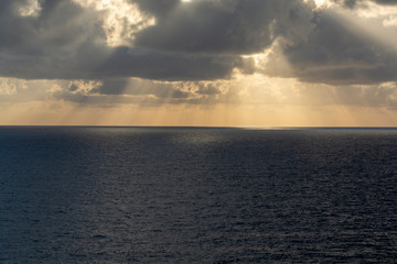 Dramatic sunset over sea water with gray clouds and sun lights