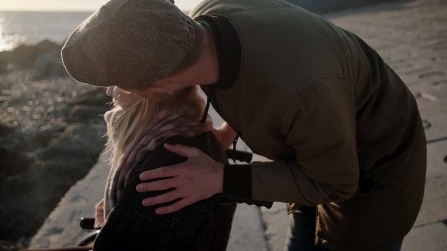 Man is stroking head of his beloved woman in wheelchair on sea coast
