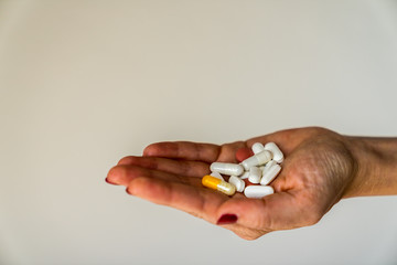 Many pills in different colors presented on open hand of a girl with red fingernails and white background