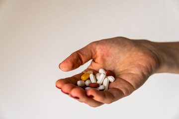 Pretty hand of a girl with red fingernails holding lots of colorful pills with vitamins for good health on white background