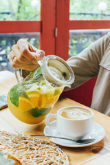 Meeting friends in summertime cafe together young woman pouring citrus tea while having lunch, background