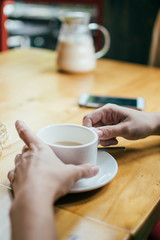 The girl drinks coffee in a cafe and touches the cup with her hands, close-up, during meeting with friend