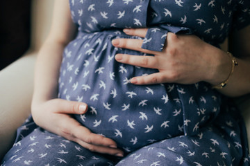 Pregnant caucasian healthy woman gently touching her belly with hands, in blue dress, close-up, background