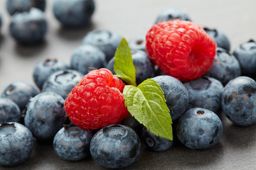 Macro photo of a bunch of wild berries in backlight, useful natural raspberry and blueberry berries close up on a stone background with bokeh