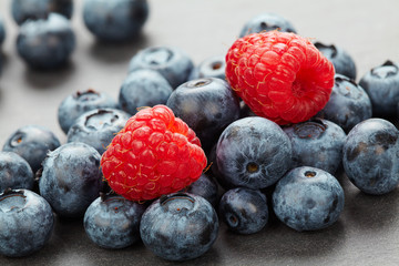 Macro photo of a bunch of wild berries in backlight, useful natural raspberry and blueberry berries close up on a stone background with bokeh