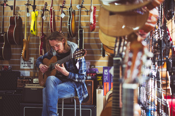 Mężczyzna gra na gitarze w sklepie muzycznym - obrazy, fototapety, plakaty