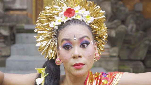 Closeup of pretty balinese dancer dancing and smiling at the camera in the temple