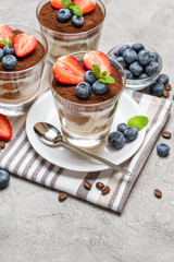 Classic tiramisu dessert with blueberries and strawberries in a glass on concrete background