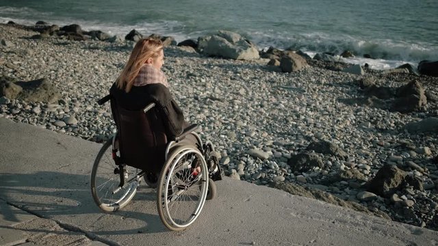 Woman with disabilities is sitting in invalid carriage and looking on sea