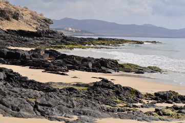 Rocky ocean beach with mountains on background. Costa Calma, Fuerteventura, Canary Islands