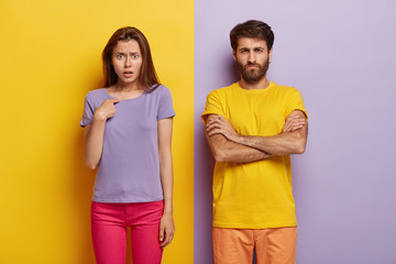 Dissatisfied sullen unshaven guy keeps arms folded, indignant young woman points at herself, asks...