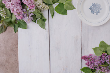 A plate and a decor of flowers on a background of white-painted wooden boards. Vintage background with lilac flowers and a place under the text. View from above. Cutlery.