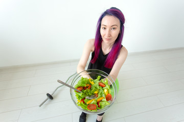 Top view of a young asian hipster girl eating a light vegetable salad after a workout at her home. Concept of losing weight and healthy lifestyle.